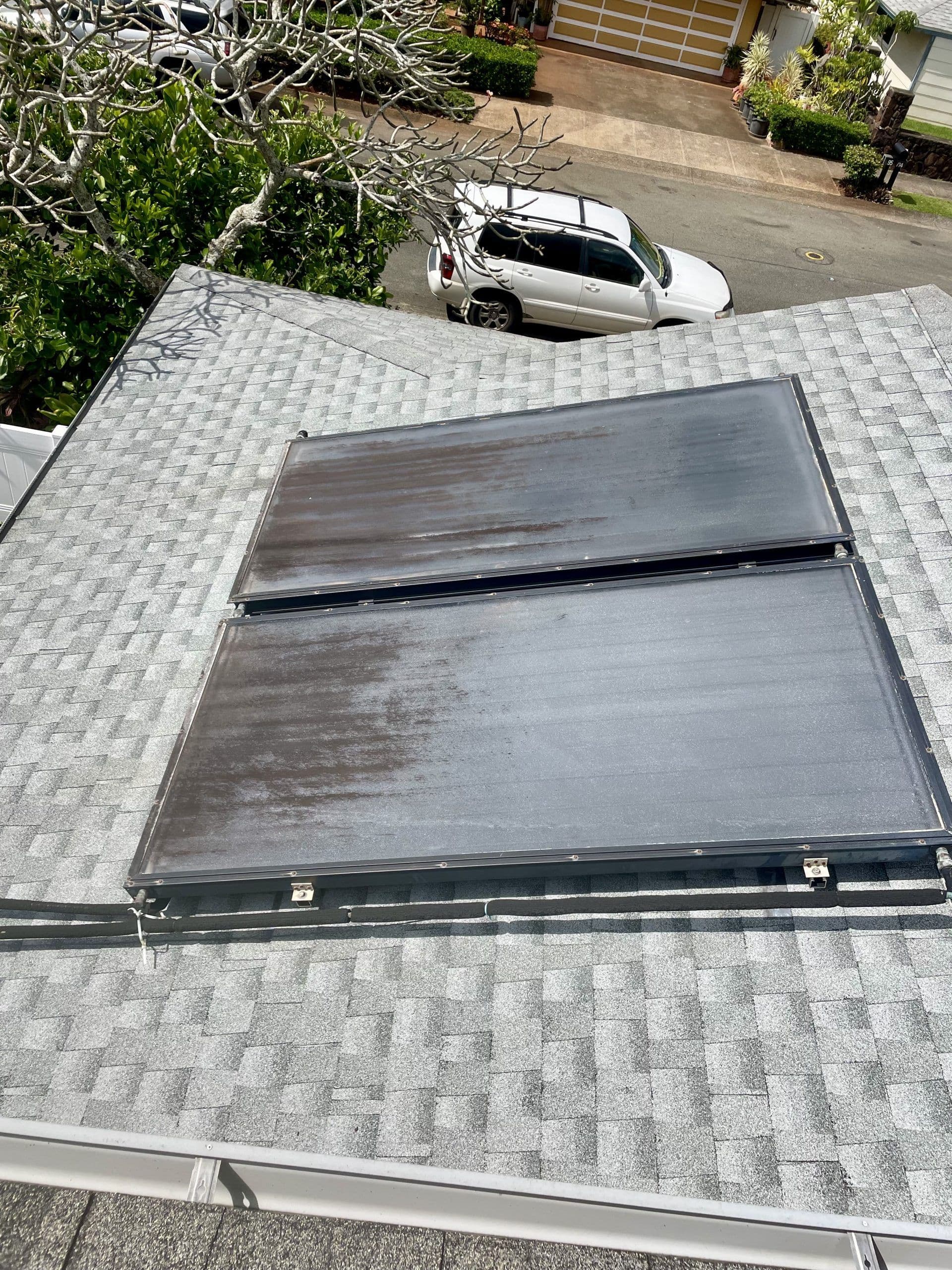 Solar panels installed on a gray shingle roof with a car parked on the street below.